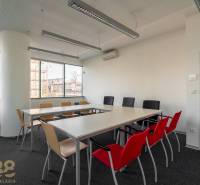 Interiér kanceláře s dlouhým stolem, barevnými židlemi a velkými okny.