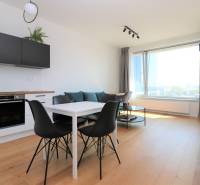 Kuchyně a jídelní stůl s černými židlemi v dvoupokojovém bytě s podlahou s dřevěným dekorem.