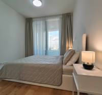 Ložnice v 2pokojovém bytě s postelí, nočním stolkem a podlahou s dřevěným dekorem.