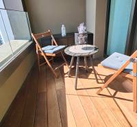 Balkon s podlahou s dřevěným dekorem, posezení a okrasný stůl v 2-pokojovém bytě.