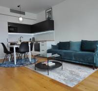 Obývací pokoj s kuchyňským koutem, tyrkysovou sedačkou, dřevěným dekorem a jídelním stolem.