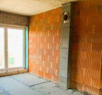 Nedokončený interiér budovy se surovými cihlami a velkými okny přináší potenciál útulné chaty.