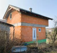 Chata ve výstavbě s cihlovými stěnami u vesnice a zahrady v pozadí.