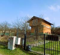 Na obrázku je chata obklopená stromy a plotem na travnatém pozemku.