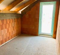 Podkrovní pokoj s cihlovými stěnami, dřevěnými trámy a světlem prosvětlená chata.