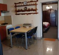 Jídelní stůl se židlemi v rodinném domě, kuchyňská část a otevřené dveře do ložnice.