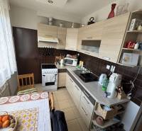 Kuchyně ve 4-pokojovém bytě s linkou, sporákem, dřevěnými skříňkami a kulatým stolem.