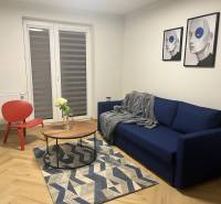 Obývací pokoj v 3pokojovém bytě s modrou pohovkou, červeným křeslem a podlahou s dřevěným dekorem.