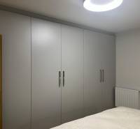 Ve 3pokojovém bytě jsou šatní skříně s bílými posuvnými dveřmi a postelí.