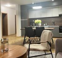 Obývací pokoj v třípokojovém bytě s kuchyní, stolem a podlahou s dřevěným dekorem.