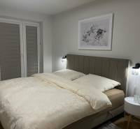 Ložnice v 3-pokojovém bytě se světlou postelí a jemným dekorem na stěně.