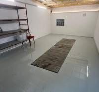 Garáže s regály a světlými stěnami, podlaha s jámou na opravu vozidel.