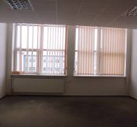 Kancelář s velkým oknem, žaluziemi a podlahou s dřevěným dekorem.