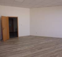 V kanceláři s podlahou s dřevěným dekorem jsou bílé stěny a otevřené dveře.