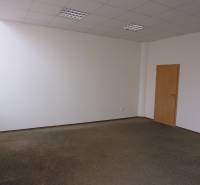 Kancelář s kobercovou podlahou, bílé stěny, dřevěné dveře; jednoduchý design.