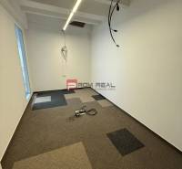 Kanceláře s barevným kobercem, bílé stěny, kabely ze stropu.