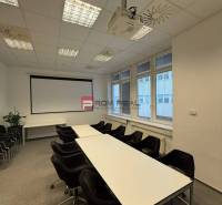 Konferenční místnost v kancelářích s projektorem, stoly a židlemi, připravená na setkání.