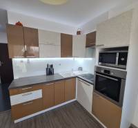 Kuchyně 2pokojového bytu s podlahou s dřevěným dekorem a moderními spotřebiči.