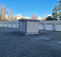 Řadová garáž v Komárně s uzavřenými branami na zpevněném povrchu za slunečného počasí.