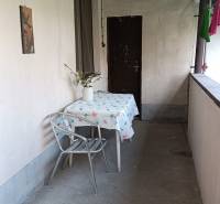 Zastřešená terasa rodinného domu, stůl se židlí, váza s květinami, obytný prostor.