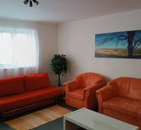 Obývací pokoj v rodinném domě s oranžovou sedačkou, křesly a obrazem krajiny.