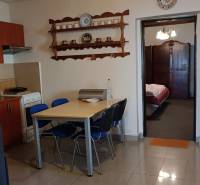 Jídelní kout a kuchyň v rodinném domě s poličkou a stropním ventilátorem.