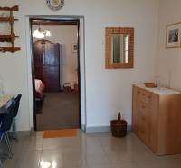 Interiér rodinného domu s dlažbou, dřevěnou komodou a stropním ventilátorem.