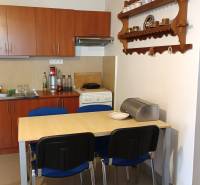 Jídelna v rodinném domě s kuchyňskou linkou, stolem a policí na stěně.