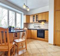 Kuchyně v 2-pokojovém bytě s dřevěným nábytkem a dlažbou, velká okna.