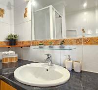 Koupelna v 2-pokojovém bytě s keramickými obklady, umyvadlem a skleněnou policí.