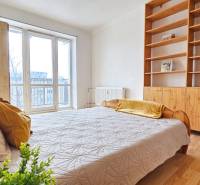 Světlá ložnice v 2-pokojovém bytě s postelí, policovou skříní a podlahou s dřevěným dekorem.