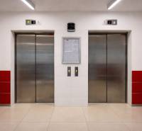 Dva výtahy se šedými dveřmi a bílými stěnami s červenými obklady.