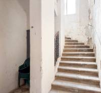 Schodiště v rodinném domě s hromadou plastových židlí. Opotřebované stěny.