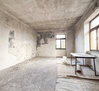 Opuštěná místnost s poškozenými stěnami a podlahou s dřevěným dekorem v rodinném domě.