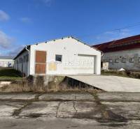 Exteriér skladů a hal v Rybkách s bílou fasádou a dřevěnými dveřmi.