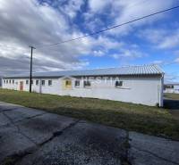 Bílá budova skladů a hal v Rybkách, obklopená trávou a betonovým chodníkem.