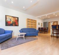 Obývací pokoj s modrými sedačkami, barevným obrazem a podlahou s dřevěným dekorem ve 3pokojovém bytě.