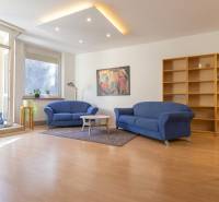 Obývací pokoj v 3pokojovém bytě s modrými sedačkami a podlahou s dřevěným dekorem.