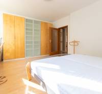 Světlá ložnice ve 3-pokojovém bytě s podlahou s dřevěným dekorem a prostornou skříní.