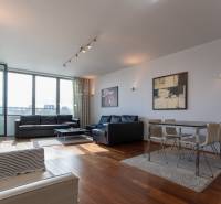 Obývací pokoj s velkými okny, podlaha s dřevěným dekorem, pohodlný nábytek a jídelní kout.