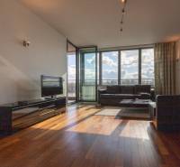 Obývací pokoj v dvoupokojovém bytě s podlahou s dřevěným dekorem a velkými okny.