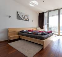 Ložnice v dvoupokojovém bytě s podlahou s dřevěným dekorem a prostornými okny.