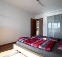 Ložnice ve dvoupokojovém bytě s podlahou s dřevěným dekorem, postelí a skříní.