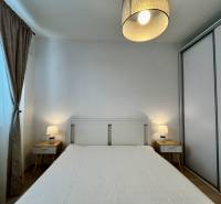 Ložnice v 2pokojovém bytě s bílou postelí, nočními stolky a lampami.