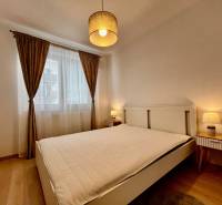 Ložnice s velkou postelí, závěsy a podlahou s dřevěným dekorem v 2-pokojovém bytě.