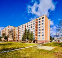 Panelový dům na sídlišti Rúbanisko II v Lučenci obklopený zelení a lavičkami.