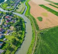 Řeka obklopená vesnicí a poli v Černé Vodě se zemědělskými a lesními pozemky.