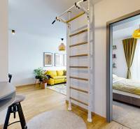 Interiér 3-pokojového bytu s podlahou s dřevěným dekorem, žebřinou a výhledem do ložnice.