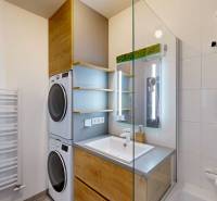 Koupelna v 3-pokojovém bytě s pračkou, sušičkou, umyvadlem a proskleným sprchovým koutem.