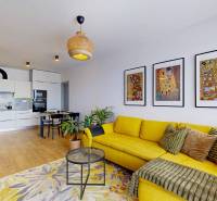 Obývací pokoj s kuchyní ve 3-pokojovém bytě, žlutá sedačka, podlaha s dřevěným dekorem.